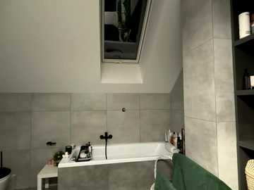 Video of a modern, minimalist bathroom with a white bathtub, grey tiled walls, black fixtures, a skylight, and a green towel hanging on a shelf.