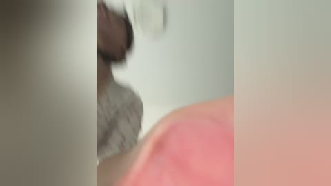 A blurry video of a person with a white headband, wearing a patterned shirt, standing in front of a white wall with a pink object in the background.