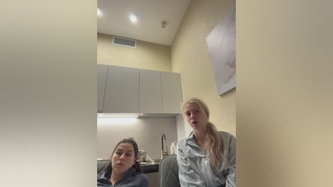 Video of two women in a modern, beige-toned kitchen. One with dark hair, another with blonde ponytail, both in casual clothing.