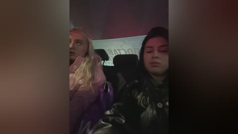 Video of two people seated on a plane, one wearing a pink jacket, the other in a black leather jacket. The background is dimly lit, with blurred text and red and purple hues.