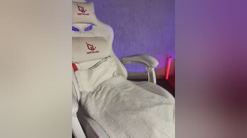 Video of a white gaming chair with red \"Gaming\" logo, covered in a white towel, in a dimly lit room with purple and red lighting accents.