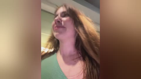 A blurry, close-up video of a woman with long, wavy brown hair, wearing a green top, seen from the side, with a blurred background.