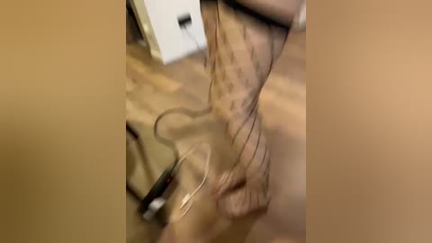 A close-up video of a man's naked, hairy body with a visible erection, standing in a dimly lit room with wooden flooring and a black electrical cord on the floor.