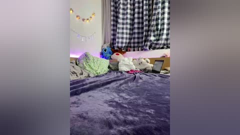 A video of a cozy bedroom with a purple blanket, stuffed toys, checkered curtains, fairy lights, and a laptop on a bed.