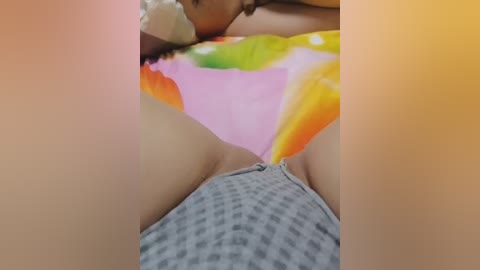 Video of a person lying on a colorful, polka-dotted blanket, wearing gray checkered shorts, with visible cleavage and a hint of a tan line.