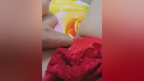 Close-up video of a person's hand delicately touching a vibrant, multicolored fabric. The hand has a light skin tone, and the fabric features bright hues of yellow, orange, and red. The background is blurred, focusing attention on the interaction between hand and fabric.
