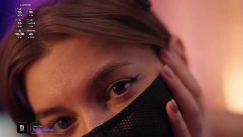 Close-up video of a young woman with light brown hair, partially covered by a black mask, focusing on her left eye, with a blurred background.