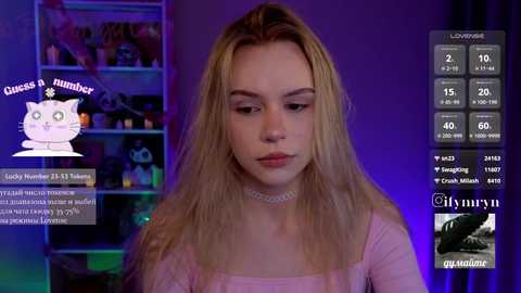 Video of a young Caucasian woman with long, blonde hair, wearing a pink top and choker, standing in a dimly-lit room with a shelf of toys and a \"Glamour\" watermark.