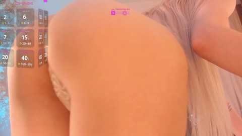 Video of a woman's bare buttocks, tan skin, partially visible in a beige top, blurred background with numbers and \"Bella\" text.
