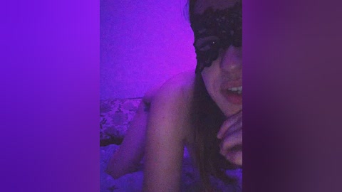 A dimly lit, grainy video captures a partially visible, topless woman with long hair and a black mask, against a purple-hued backdrop, creating a mysterious, sensual atmosphere.