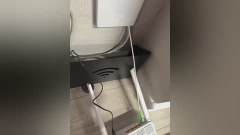 Video of a modern living room corner, featuring a black wireless charging stand with a smartphone, a white power strip, and a white wall-mounted television. The room has beige carpet and light wood flooring.