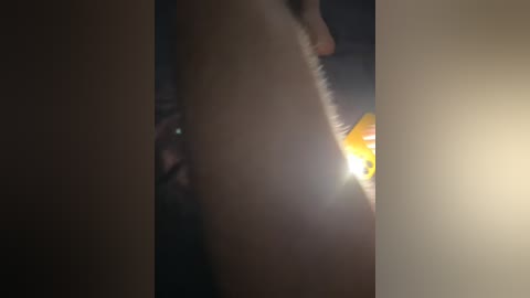 A dimly lit, close-up video shows a naked woman's body with a bright light shining from the right. Her skin is pale, and her figure is partially obscured by the shadows.