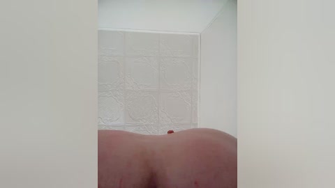 Video of a close-up view of a person's bare buttocks from behind, set against a white tiled bathroom wall with a textured pattern. The person has light skin, and the focus is on the smooth, rounded shape of the buttocks.