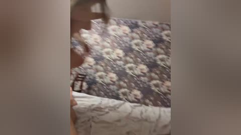 A blurred video shows a person in motion, holding a fluffy pillow against a patterned wall. The pillow is white with a soft texture, and the wall features a floral design in muted colors. The person's face is out of focus.