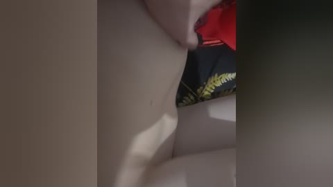 A close-up video of a light-skinned person's torso, with a mole on the left side, partially covered by a red garment. The background features a black and yellow patterned fabric.