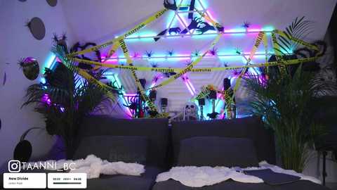 Video of a dimly lit room with a black sofa, yellow caution tape, neon lights, skulls, and potted plants, giving a spooky, abandoned vibe.