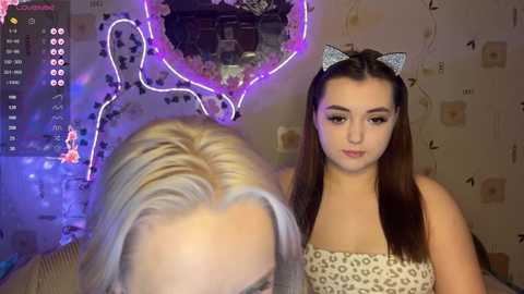 Video of a young woman with fair skin, long straight brown hair, and light makeup, wearing a leopard print bandeau top, and a glittery cat ear headband. Background includes a mirror, fairy lights, and a cozy, softly lit room with a playful, whimsical atmosphere.
