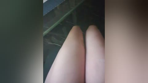 Video of a pair of light-skinned, slender legs with smooth skin, partially visible from the knees down, positioned next to a dark green, textured surface with a marble-like pattern.