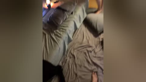 Video of a dimly-lit bedroom with a person lying on a bed, wearing gray pajamas, under a gray blanket, with a lit candle beside them.