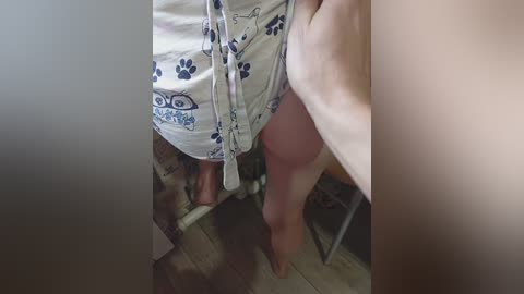 A video of a person in a white robe with blue paw prints, standing on a wooden floor, with a blurred background.