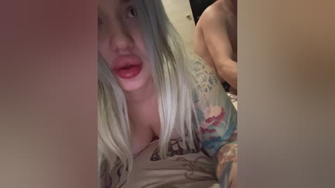 Video of a young, fair-skinned woman with long, platinum blonde hair, wearing a floral-patterned top, leaning forward with parted lips, partially obscured by a shadow.