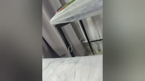 A video showing a hospital bed with a white sheet, a gray curtain partially covering the bed frame, and a black metal bar attached to the ceiling. The image appears to be taken from an overhead perspective.