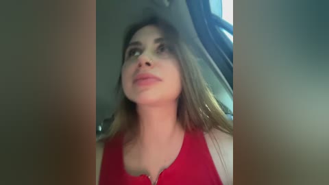 A video of a young woman with light skin and long, straight brown hair, wearing a red tank top, taken from a car's rear-view mirror.