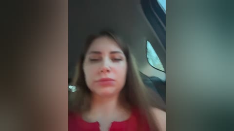 Video of a woman with light skin and shoulder-length blonde hair, wearing a red dress, looking relaxed with eyes closed in the backseat of a car.