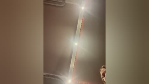 Video of a man in a dimly lit room with a large, bright light source creating lens flare effects in the background. The man's face is partially visible, and the room has a warm, muted color palette.