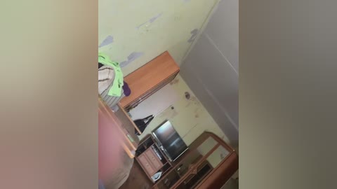 Video of a cramped, dimly lit room with a small bed, a desk, and a TV. The walls are peeling, and a green bag is on the floor.