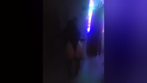 A dimly lit video captures a person, likely male, with dark hair, wearing a black shirt, standing in front of a blue and purple-lit bar, possibly in a nightclub or a dimly-lit room.