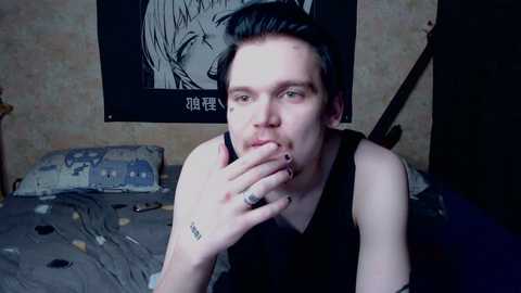 Video of a pale-skinned, short-haired man with tattoos, smoking, sitting on a messy bed with a Japanese anime poster on the wall.
