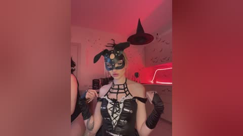 Video of a woman in a dark, black-and-red room, wearing a bunny mask, black corset, and wrist cuffs. She holds a whip and stands in front of a black wall with a red neon light.