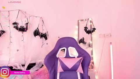 A video of a purple gaming chair with a bat motif, surrounded by fairy lights, bat decorations, and a mirror. The room has a pinkish glow, giving it a whimsical, Halloween-themed ambiance.