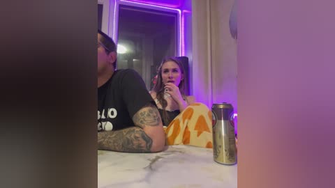 Video of a tattooed woman with long brown hair in a cozy room, sipping coffee, wearing a black shirt and orange pants.