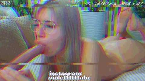Video of a young woman with glasses, nude, on a couch, performing oral sex on a man, vibrant colors, text overlay, digital filter.