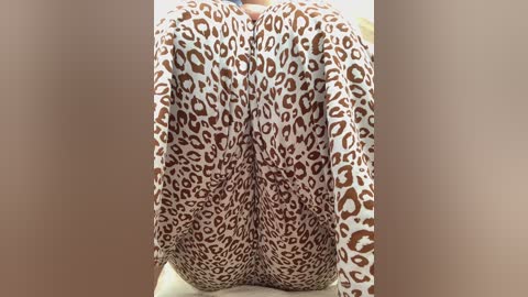 A video of a person's buttocks, clad in leopard print leggings, positioned between two vertical beige walls, creating a focal point on the patterned fabric.
