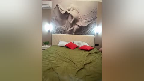 Video of a modern bedroom with beige walls, a large relief artwork of a woman's face, a green bedspread, two red pillows, and two wall-mounted lights.