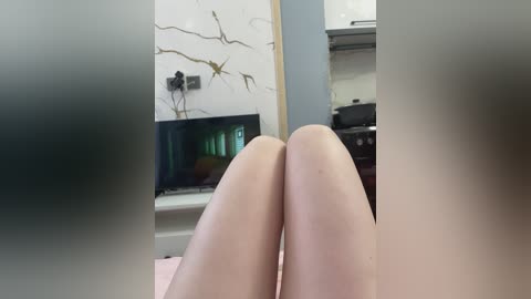 Video of a woman's smooth, pale legs reclining on a bed, with a white marble-patterned wall and a small aquarium visible in the background.