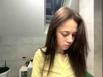 Video of a young girl with long brown hair, wearing a yellow shirt, standing in a white-tiled bathroom with a window and green toilet.