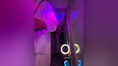 A video captures a dimly lit hallway with purple and pink lighting, revealing a person in a white robe partially obscured by the shadows.