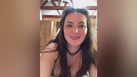 Video of a young woman with long dark hair, wearing a black choker necklace, smiling in a rustic wooden room with wooden beams.