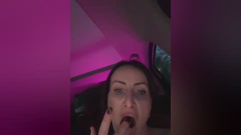 A dimly-lit video of a woman with light skin and dark hair performing oral sex on an unseen person, with pink and purple lighting creating a sensual ambiance.