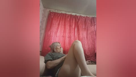 A video of an elderly woman with light skin, wearing glasses, lying on a couch with red curtains in the background.