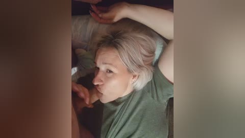 A video showing a blonde woman with fair skin performing oral sex on a man, lying on a bed with beige sheets.
