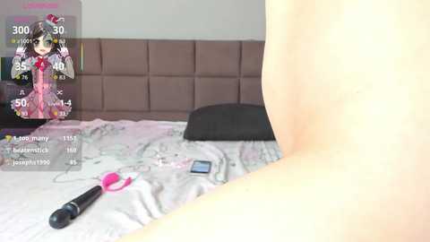 A video of a naked person lying on a bed, with a virtual avatar of a pink-clad anime girl superimposed, featuring a live-streaming overlay.