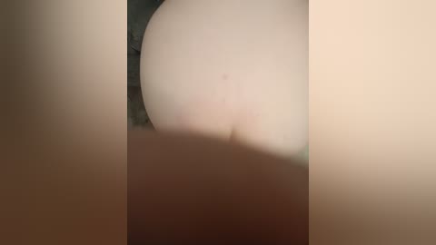 A video showing a close-up of a person's bare buttocks, framed by two vertical, out-of-focus objects, likely walls, creating a triangular composition. The skin is pale, and there are no visible tattoos or clothing.
