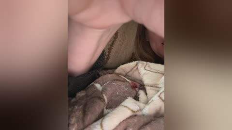 Video of a young child, possibly a baby, lying on a beige blanket with a pattern. The child's head is partially covered by a hand, likely from an adult. The setting appears to be a domestic environment, possibly a bedroom.