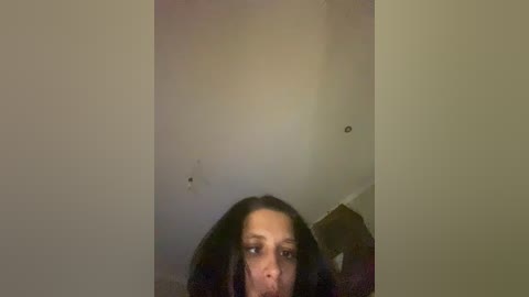 A blurry video of a woman with long black hair, partially visible, taken in a dimly lit, narrow hallway with off-white walls.