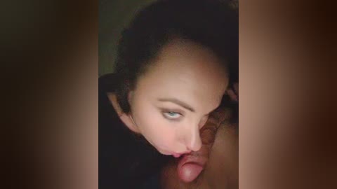 Video of a close-up of a woman with light skin, dark hair, and blue eyes performing oral sex on a man with a circumcised penis. The background is blurred, focusing attention on the intimate act.